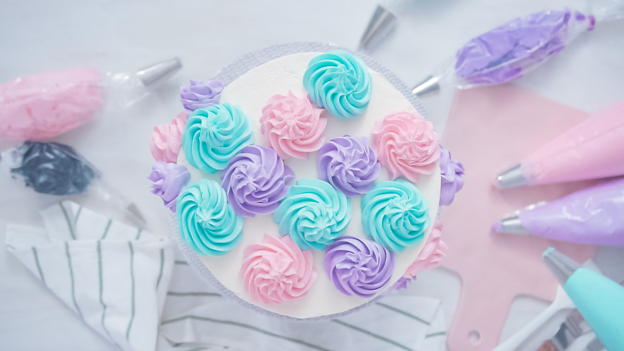 Piping pastel color buttercream rosettes on a white cake